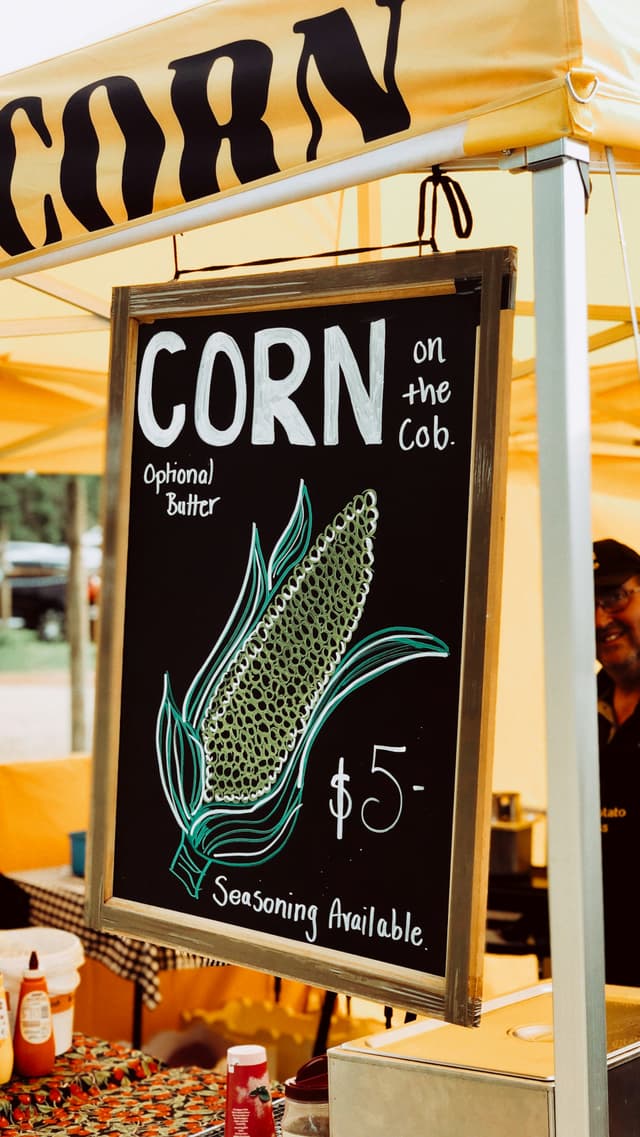 Hand-lettered chalk farm-stand sign reading 'CORN on the cob.'